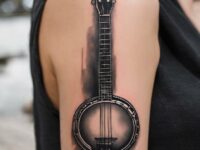 A-black-and-gray-shaded-banjo-tattoo-on-the-upper-arm