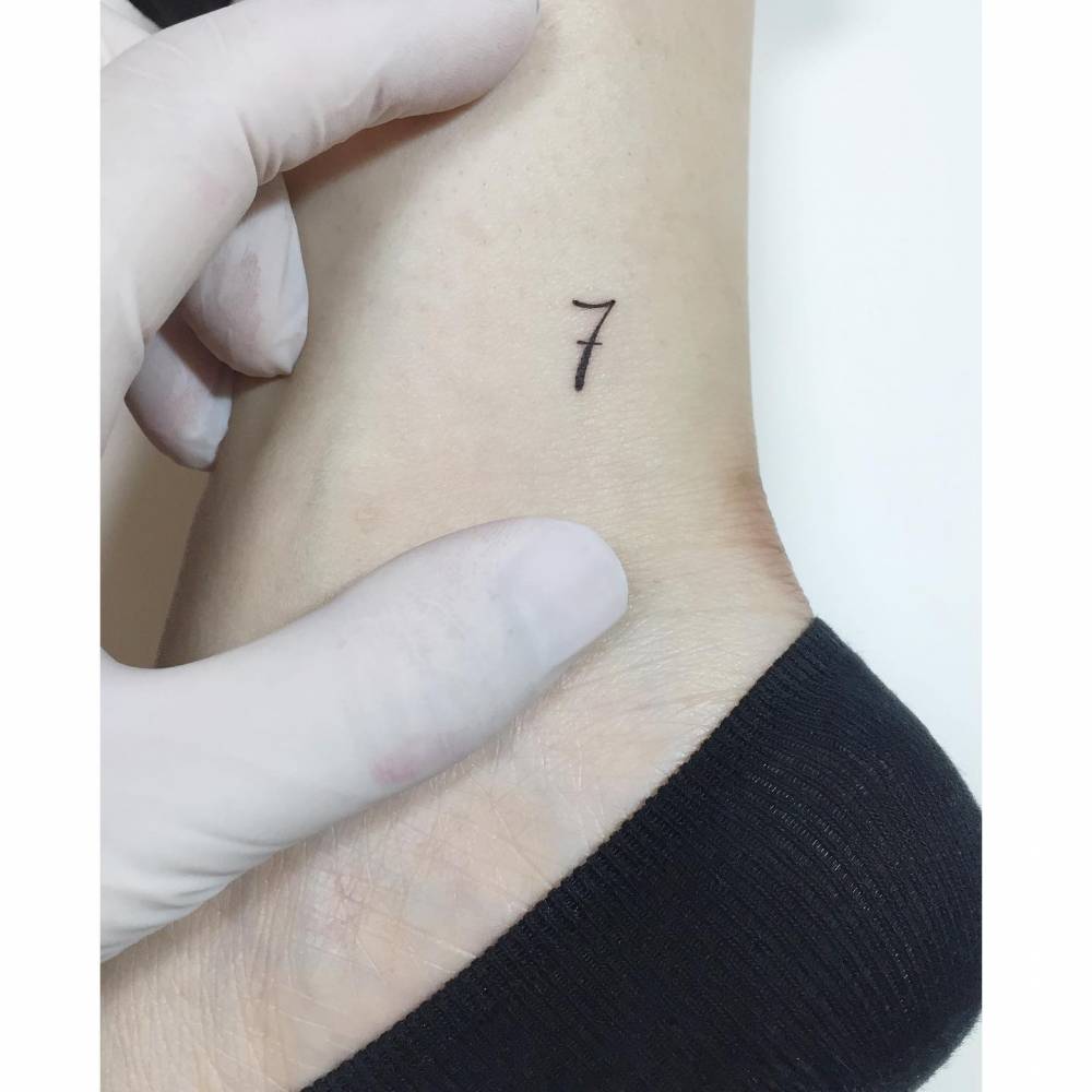 Minimalistic number '7' tattoo located on the ankle.